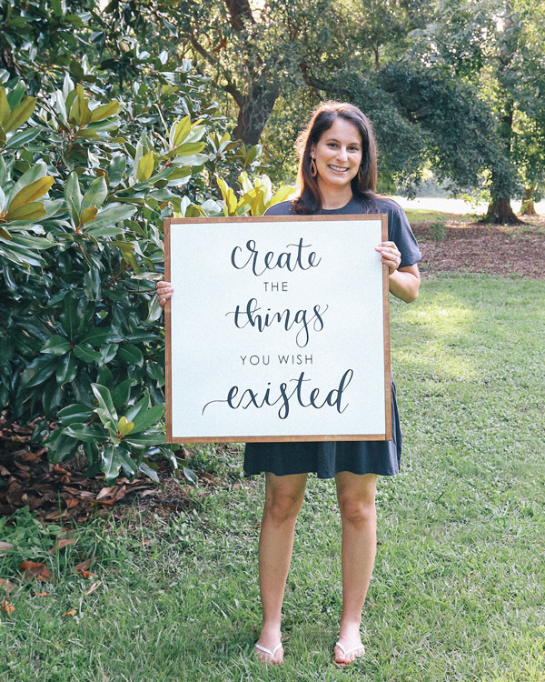 holding a DIY wood sign that says Create the things you wish existed