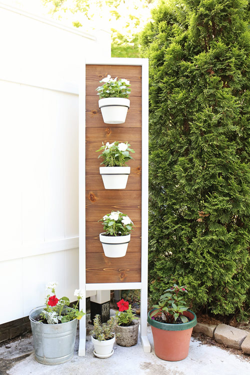 diy outdoor plant stand with flowers in front of fence and tree