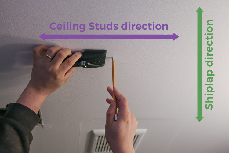 Using a studfinder on the ceiling to locate studs and mark with pencil direction of studs
