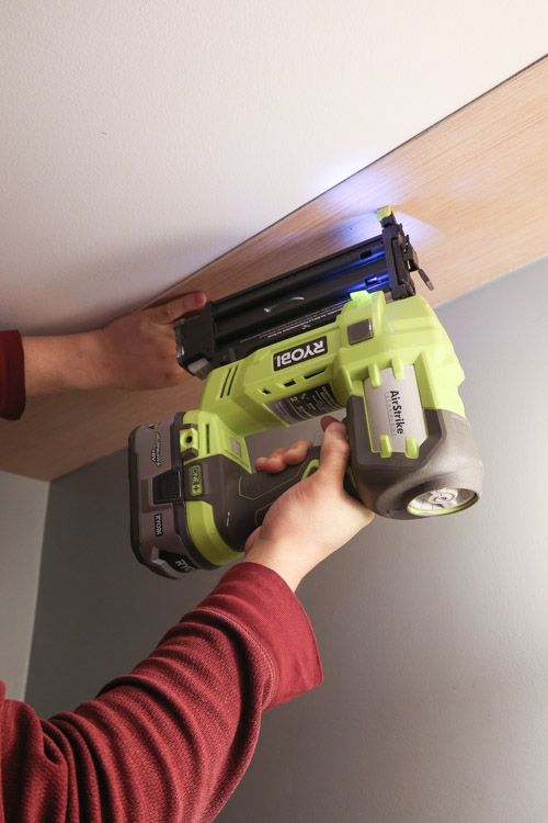 A brad nailer attaching a shiplap plank to the ceiling