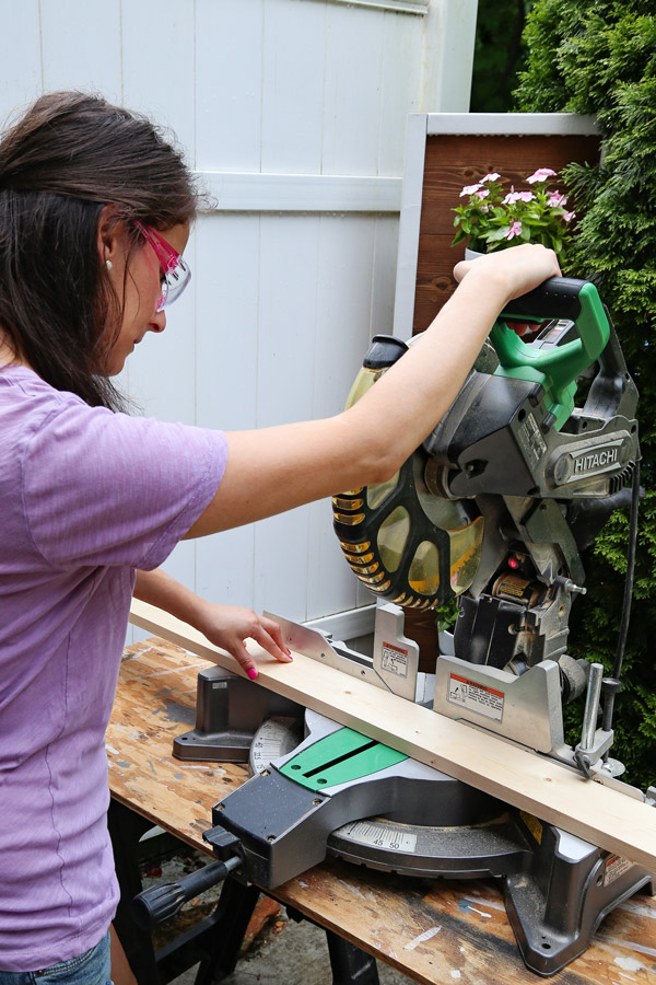 woman using a miter saw with pink saftey glasses