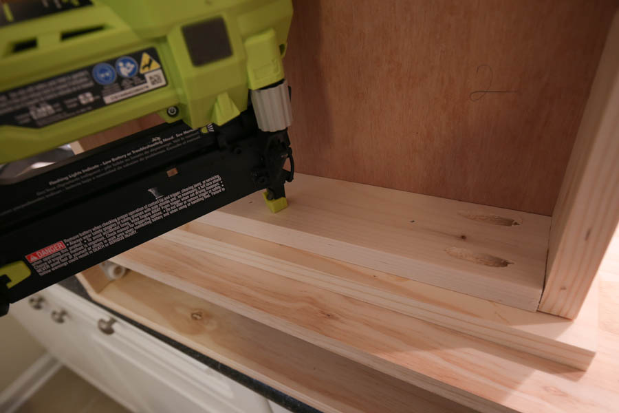 Attaching the drawer faces to the makeup vanity with a brad nailer from the inside of the drawer