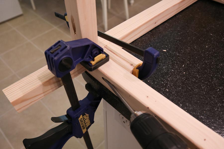 Attaching bottom leg support board brace to vanity leg sides with clamps, pocket holes, and drill