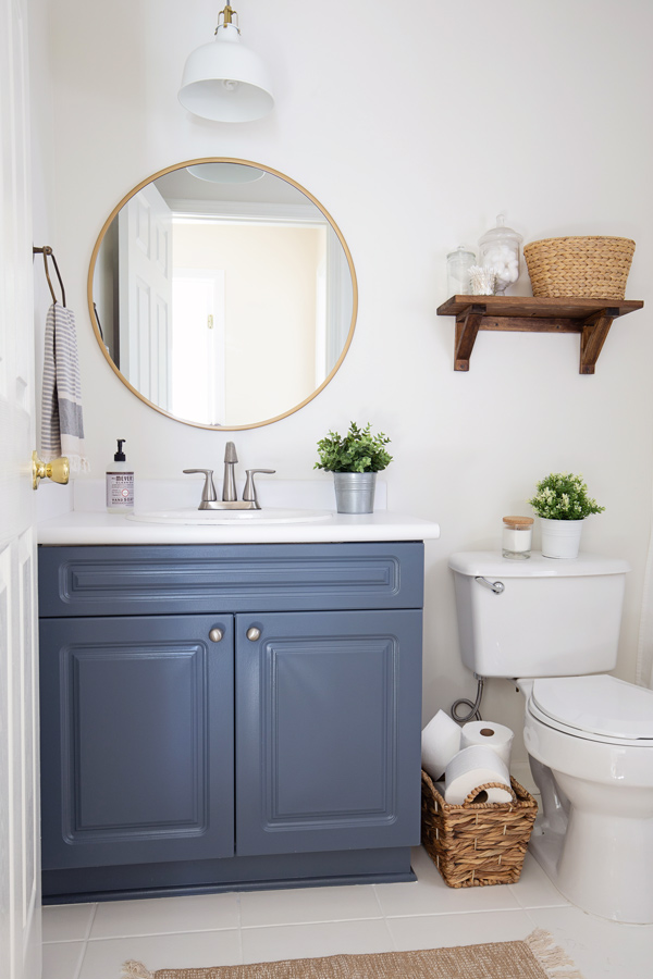 budget bathroom makeover with blue bathroom vanity, white walls, and round gold mirror