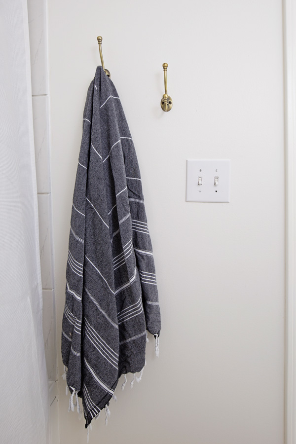 gold wall hooks on wall for bath towel storage next to the shower