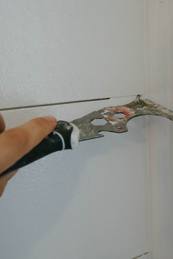 clearing excess paint out of shiplap wall gap with painter's scraper tool