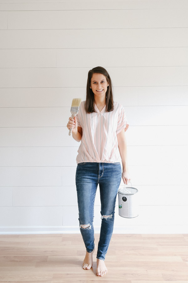 woman holding paint brush and paint can with painted shiplap wall