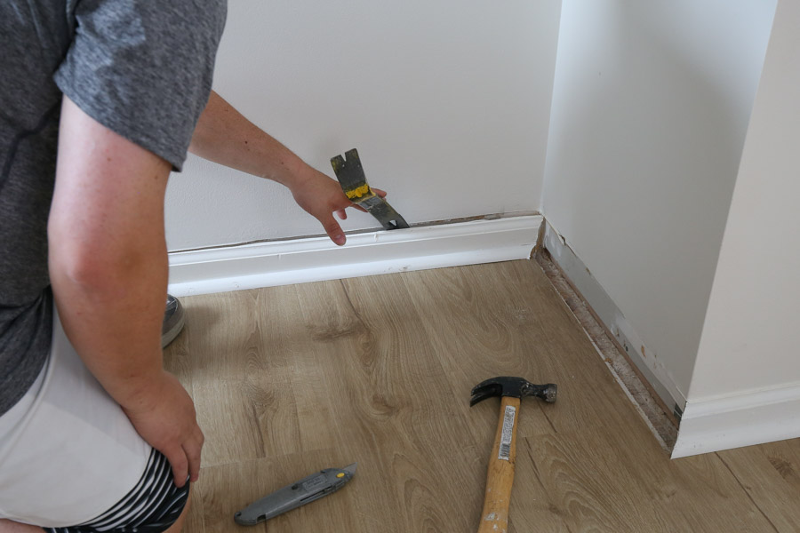 Use a prybar and hammer to remove baseboards from wall after scoring caulk line with utility knife