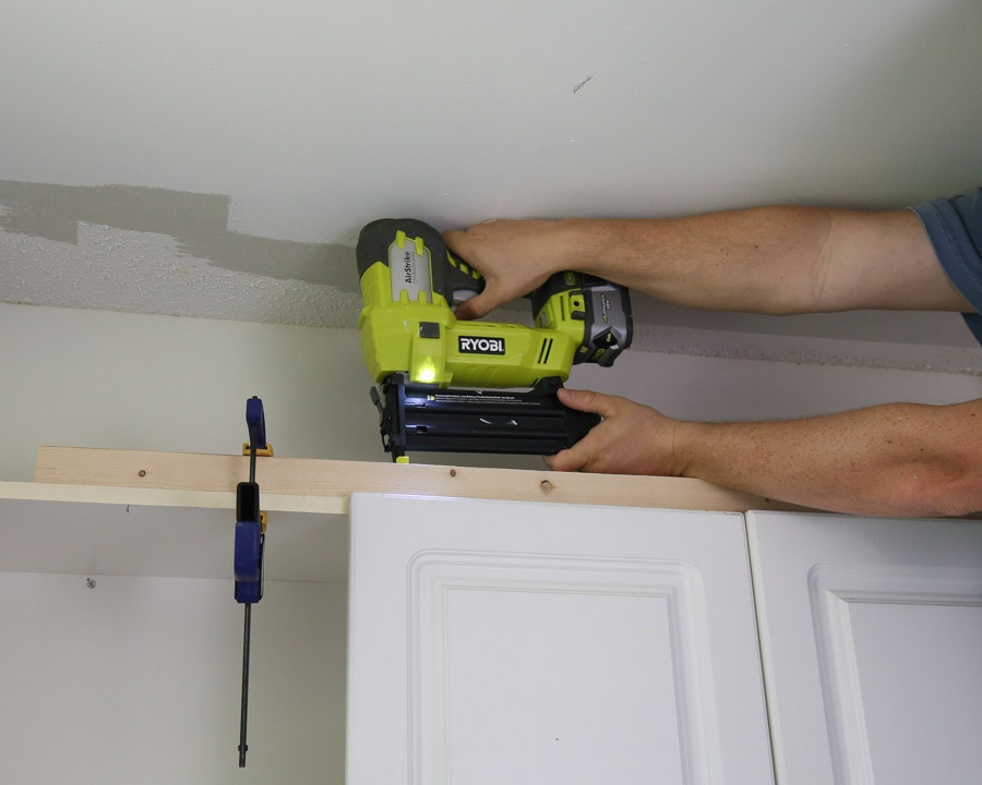 Add a 2x2 board to the top of your cabinets with 2" brad nails and a brad nailer