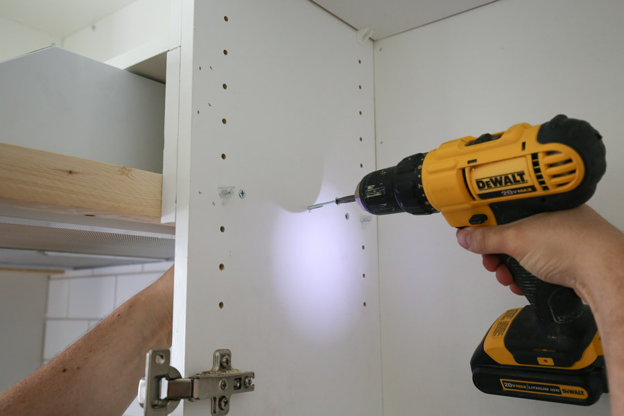 Installing range hood cover frame with drill and screws through cabinet sides