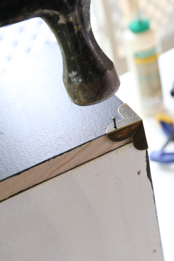 adding brass corner brackets to desk organizer with a hammer and nails