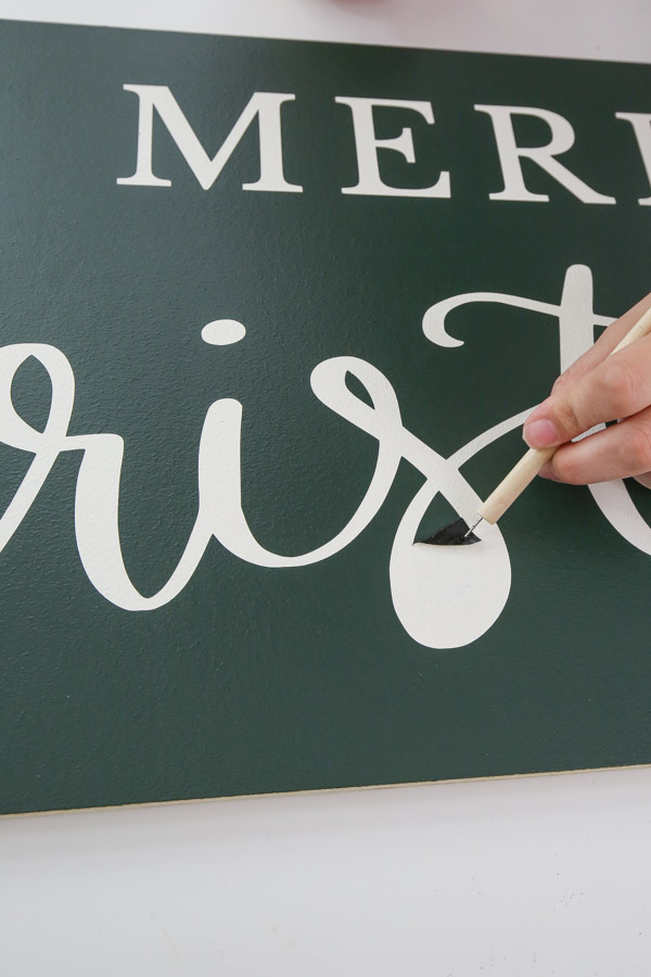 using a vinyl weeding tool to remove small parts of vinyl stencil from DIY sign