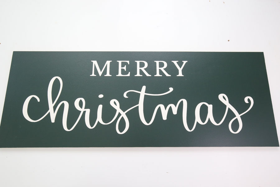 diy farmhouse christmas sign with green paint and white lettering before attaching frame