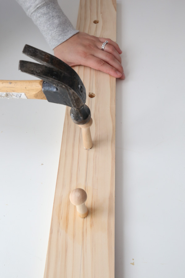 hammering shaker pegs into holes on DIY coat rack