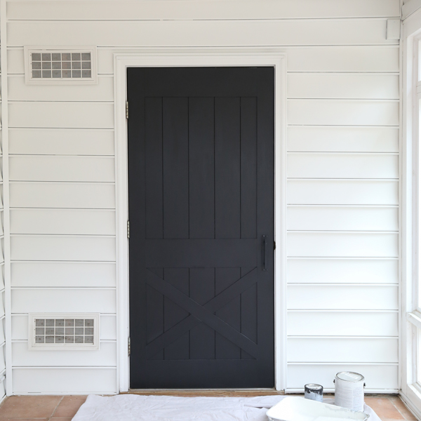 DIY faux barn door with shiplap painted black and paint can, paint tray, and drop cloth on floor