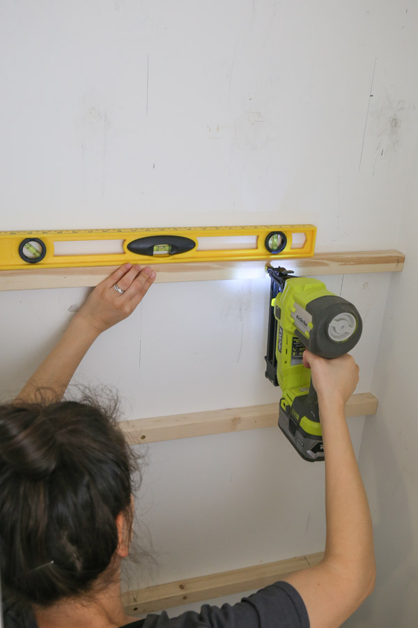 using a level and brad nailer to attach 2x2 shelf supports to wall first before screwing