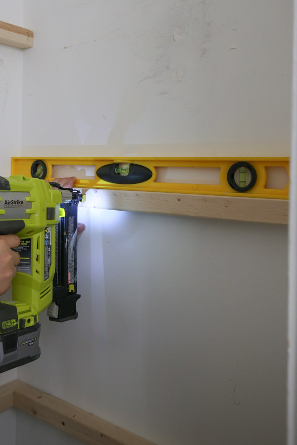 using a level and brad nailer to attach 2x2 shelf supports to wall first before screwing