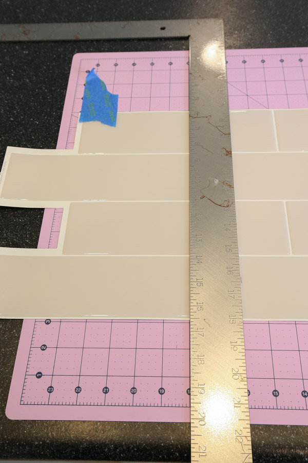 using a metal ruler and cutting mat to make a straight cut on the peel and stick tile sheet