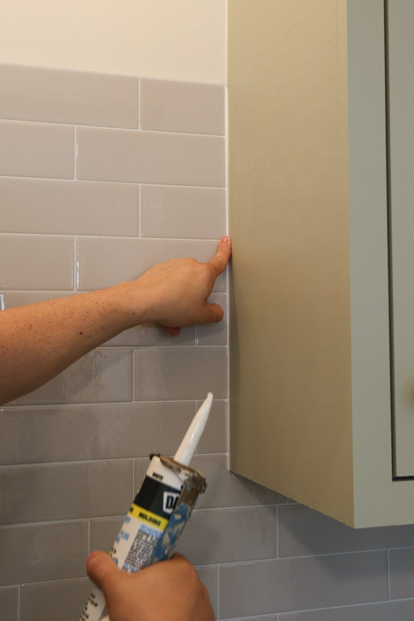 caulking the edge of the peel and stick tile and cabinet