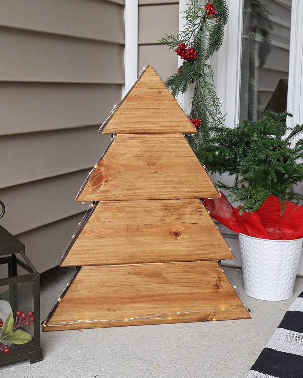 DIY wood Christmas tree with fairy string lights along edges on front porch