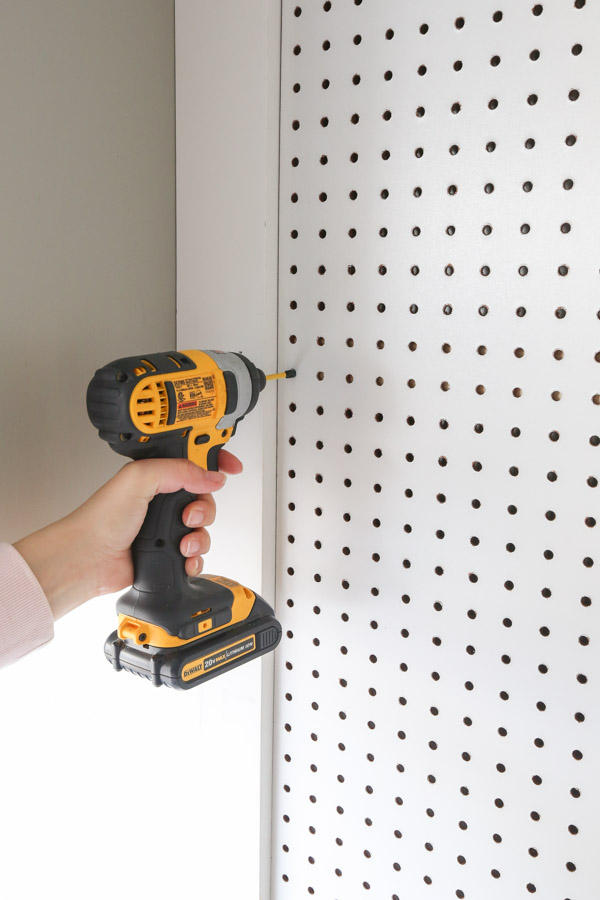 installing the pegboard panel onto the pegboard wall with a drill