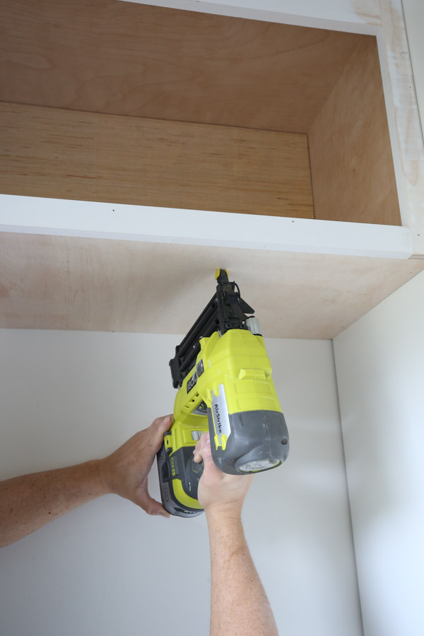 using a brad nailer to attach the bottom panel cover board to the bottom of the storage cabinet