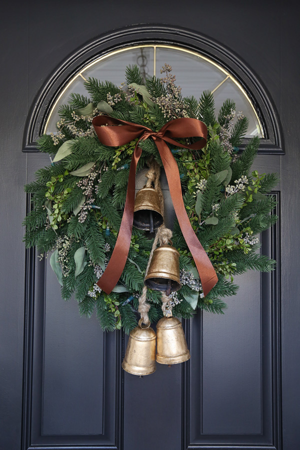 DIY minimalist Christmas wreath with brown satin ribbon and vintage brass jingle bells on front door