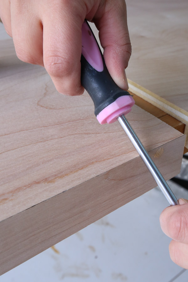 using a screwdriver shaft to rub beveled edges of DIY wood desk top together for seamless joint
