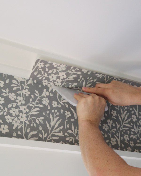 using a smoothing tool and sharp utility blade to help trim excess peel and stick wallpaper from wall