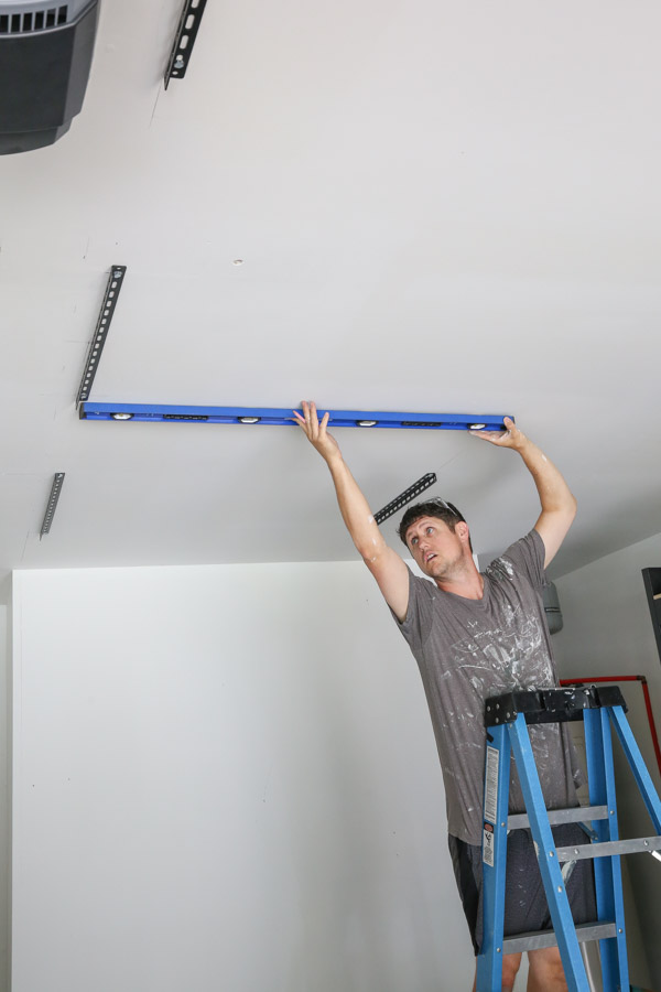 using a 4 ft level to help Install the ceiling brackets for the garage ceiling shelves diy into the ceiling joists