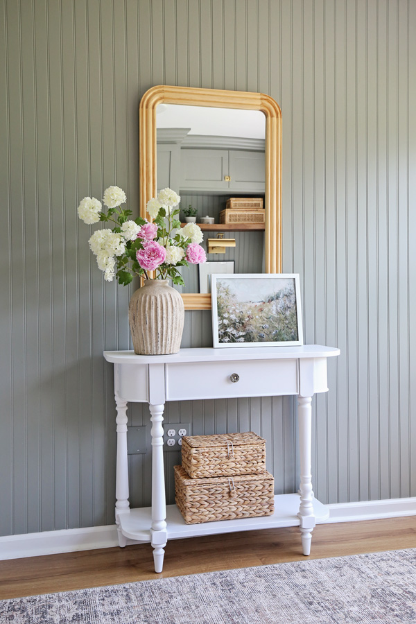 charming office wall decor ideas with vintage inspired console table, wood arch mirror, baskets, framed art, and handcrafted vase on beadboard wall painted green