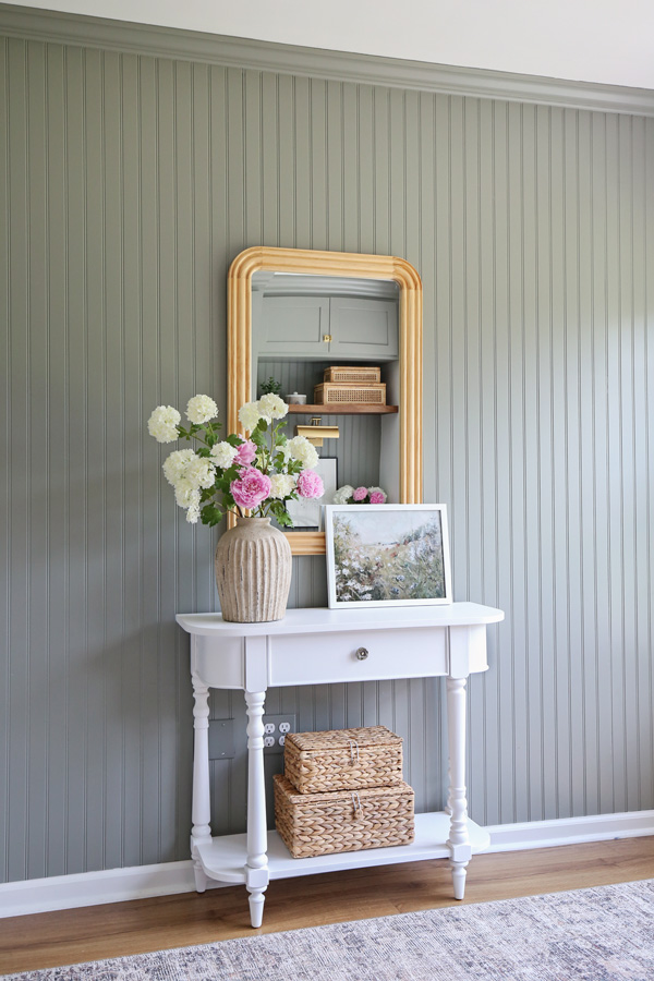 charming office wall decor ideas with vintage inspired console table, wood arch mirror, baskets, framed art, and handcrafted vase on beadboard wall painted green