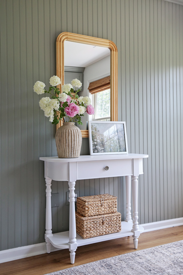 charming office wall decor ideas with vintage inspired console table, wood arch mirror, baskets, framed art, and handcrafted vase on beadboard wall